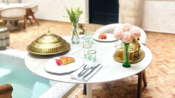 Mesa de jantar posta com bandeja de latão, copos, vaso com flores e pratos com comida.