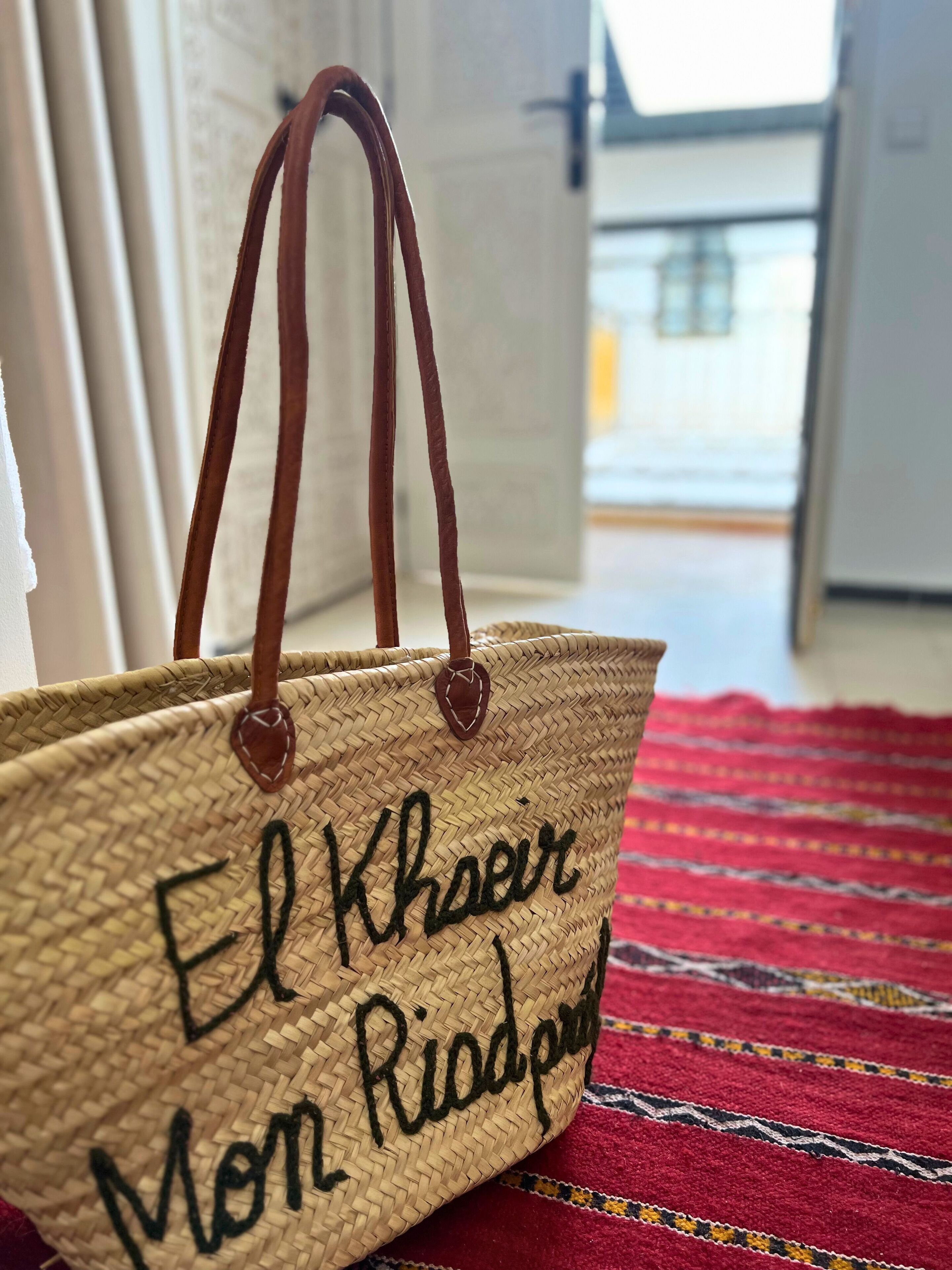Eine gewebte Tasche mit Tragegriffen und aufgestickter Schrift.