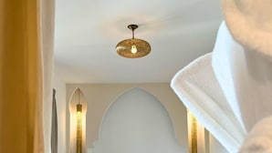Quarto de hotel com uma cama grande, um ventilador de teto e duas luminárias fixadas na parede.