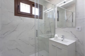 Enjoy a refreshing shower in the sleek shower area with handheld showerhead and wall-mounted faucet, accompanied by a convenient vanity with sink, towel, and mirror.