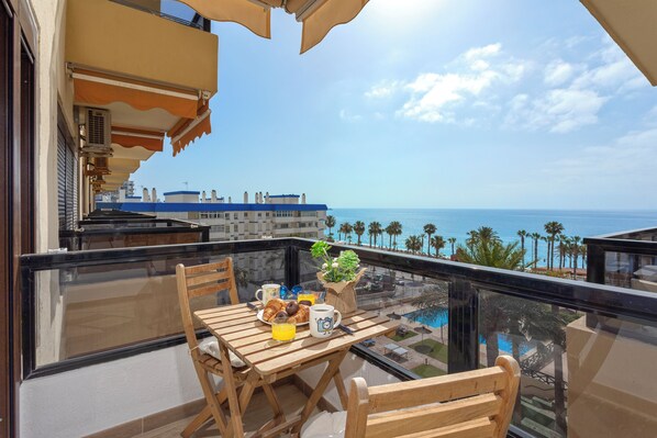 Enjoy a seaside breakfast on this balcony with a table set for two, overlooking the ocean and palm trees.