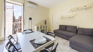 A dining area with a table set for two, a gray sofa, and a balcony with a railing. - Murales Street on Spanish Quarter (Naples)