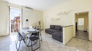 A modern apartment with a dining area, a gray sofa, and a view of the city through a large window. - Murales Street on Spanish Quarter (Naples)