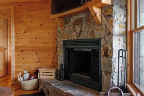 Ein gemütliches Blockhaus-Interieur mit Kamin aus Stein, Holzwänden und einem darüber hängenden Fernseher.