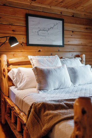 A wooden cabin interior with a bed, a map on the wall, and a lamp. - Views @ Whitepath | Mtn Views + Hot Tub + Fire Pit (Ellijay)