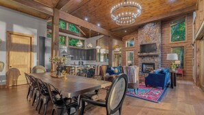 A spacious log cabin interior with a large dining table, multiple seating areas, a fireplace, and a kitchen with modern appliances. - Big Abe | Sunset Views + Hot Tub + 6BR Lodge (Blue Ridge)