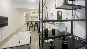 A modern interior with a dining area, a black shelving unit with decorative items, and a kitchen in the background. - Modern Studio In San Telmo With Pool - Paseo 423 (Buenos Aires)