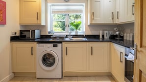 A compact kitchen with a washing machine, a microwave, a sink, and cabinets. - Shrewsbury Apartment (Shrewsbury)