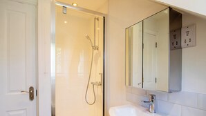 A bathroom with a glass-enclosed shower, a white sink, and a mirror above it. - Shrewsbury Apartment (Shrewsbury)