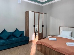 A bedroom with a bed, a wardrobe, a blue sofa, and a nightstand. - KORSAR TEMIRKAZYK (Astana)