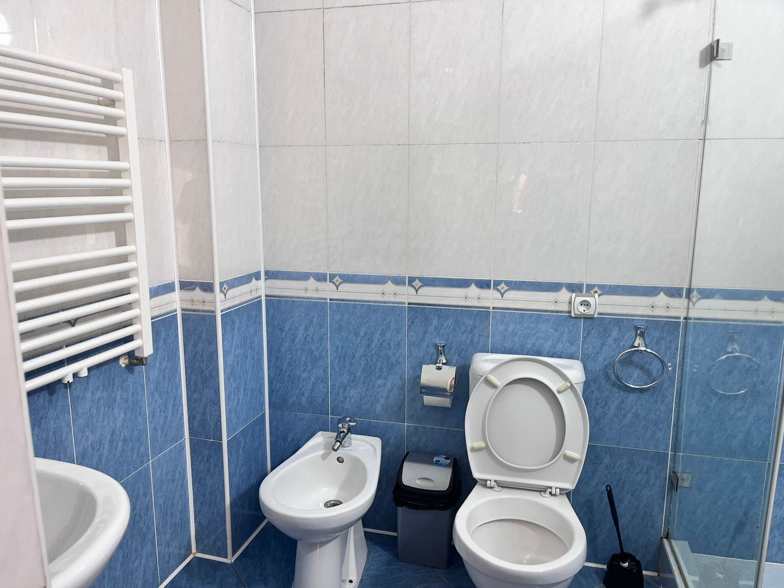A bathroom with a bidet, a toilet, a sink, and a towel rack.