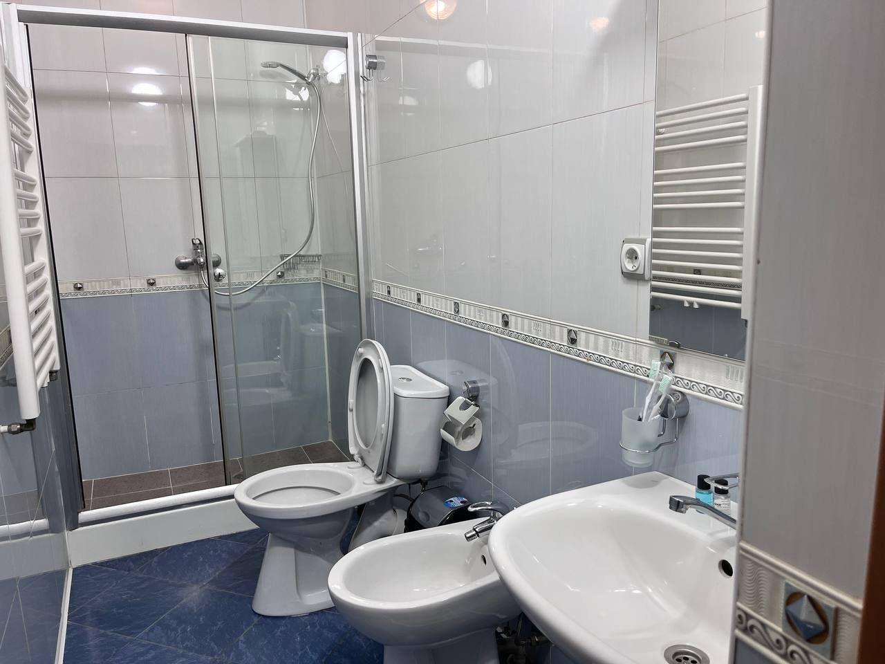 Een moderne badkamer met een douche in glazen cabine, twee toiletten, een wastafel en een handdoekrek.