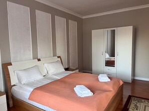 A neatly made bed with white linens and a peach-colored blanket, a wooden nightstand, and a white wardrobe with a mirror. - KORSAR TEMIRKAZYK (Astana)