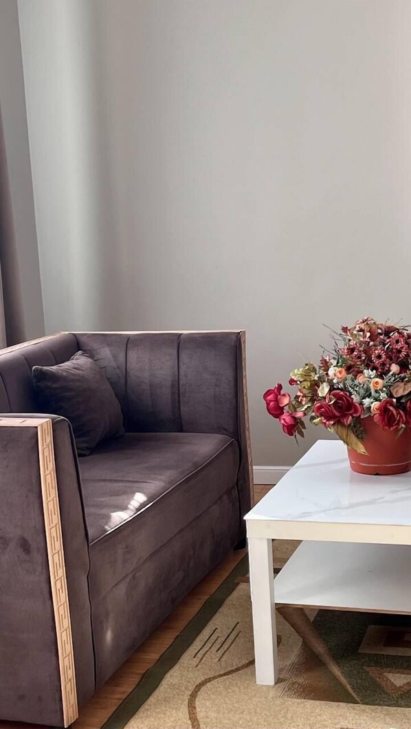 A modern living room with a dark leather sofa, a white coffee table, and a potted plant with red flowers. - KORSAR TEMIRKAZYK (Astana)