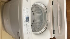 Valkoisen pesukoneen etupuoli, jossa on ohjauspaneeli, läpinäkyvä luukku ja pieni näyttö.