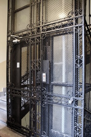 A black metal gate with intricate designs, a staircase, and a small sign on the wall. - Standard Aparmtent by Hi5 - Brody street (Budapest)