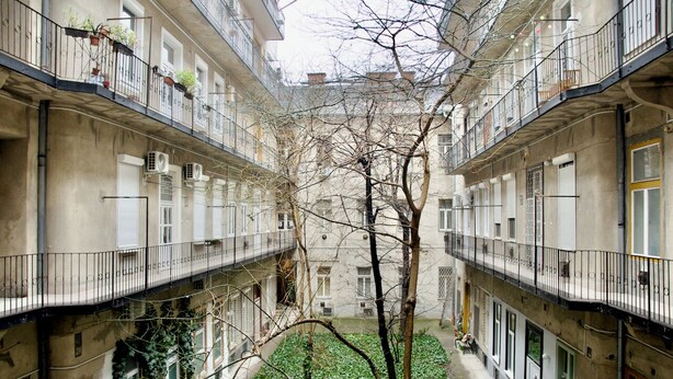 Ein Innenhof mit einem zentralen Baum, umgeben von Gebäuden mit Balkonen und Klimaanlagen.