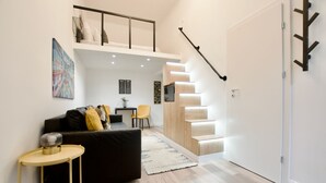 Ein modernes Wohnzimmer mit einer schwarzen Couch, einem kleinen runden Tisch, einer Treppe und einer weißen Tür.