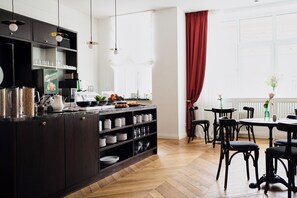 A modern kitchen with dark cabinetry, a central island, and a dining area with black chairs and a table. - Hotel Lindenufer (Berlin)