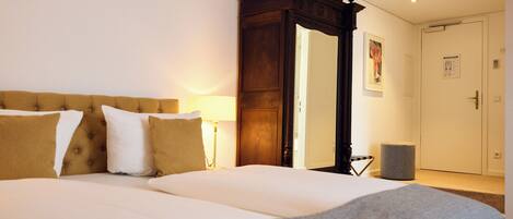 A hotel room with a large bed, a wooden headboard, a nightstand with a lamp, a wardrobe, and a mirror.