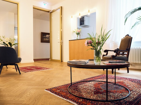 A hotel lobby with a round table, a chair, a vase with flowers, a book, and a patterned rug. - Hotel Lindenufer (Berlin)