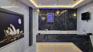 Eine moderne Hotelhalle mit einer Rezeption, Marmorwänden, einem gerahmten Kunstwerk mit dem Sydney Opera House und einem großen Bildschirm, der dasselbe Bild zeigt.