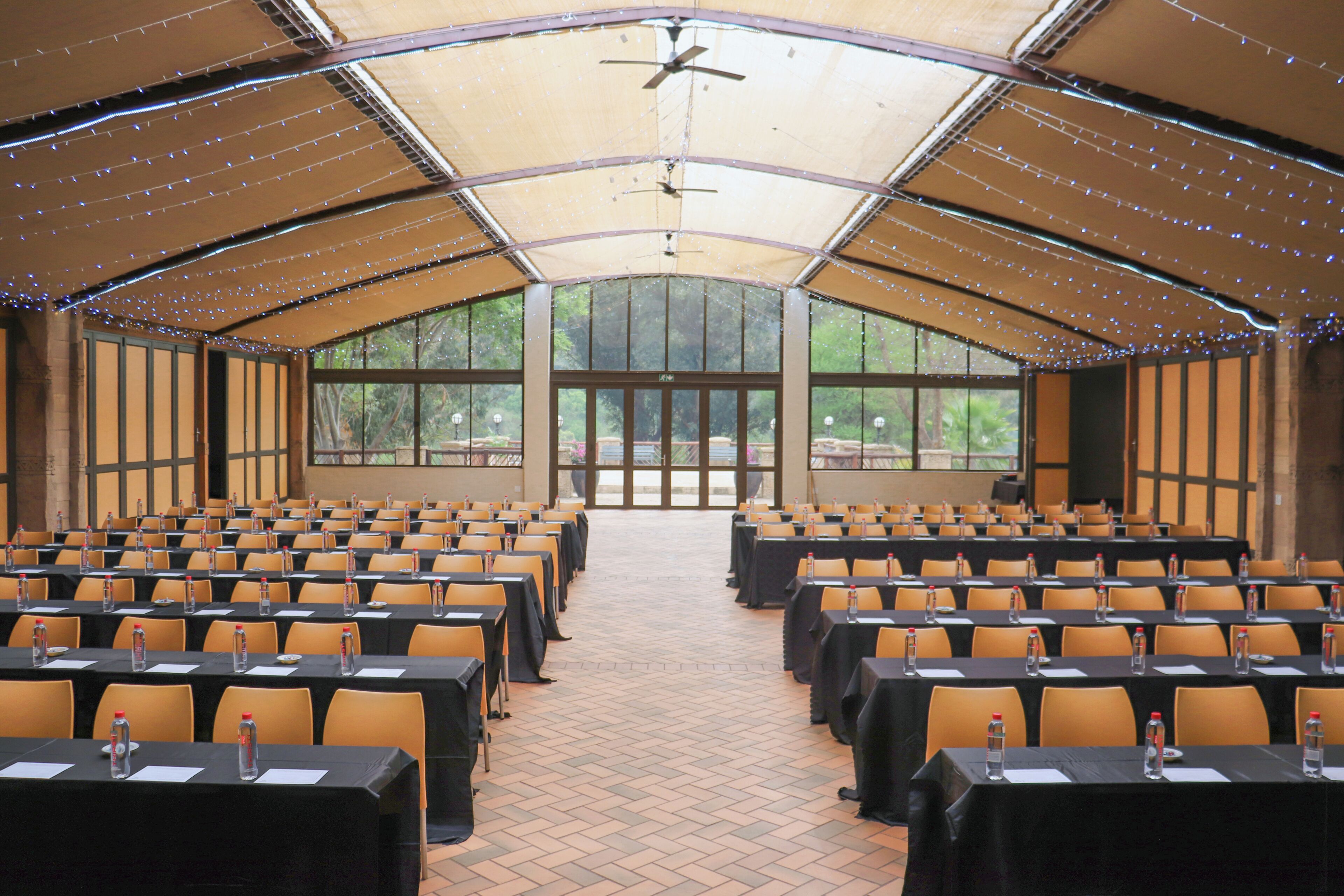 A conference room with rows of tables and chairs, large windows, and a ceiling fan.
