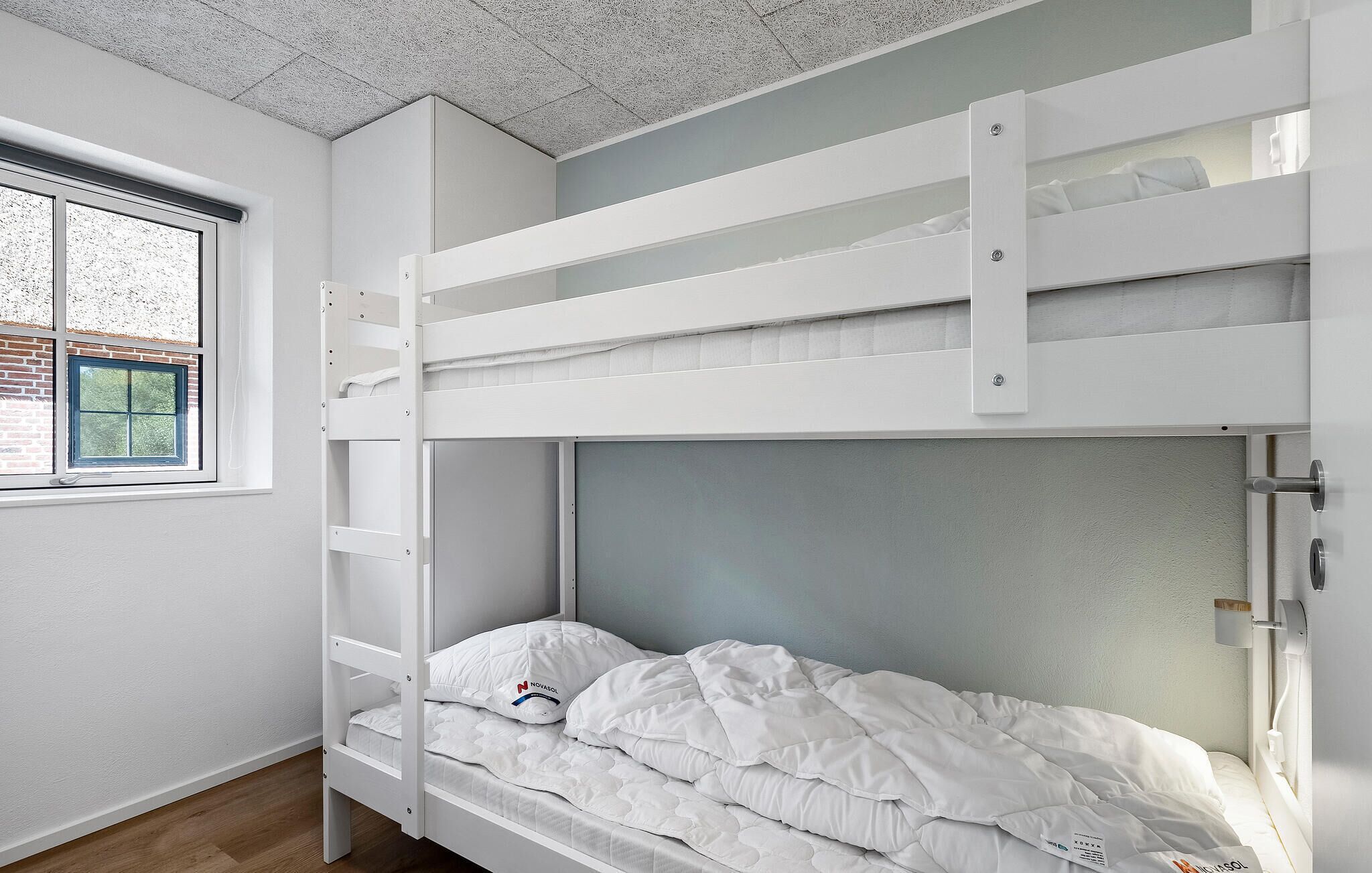 A bunk bed with white bedding and a window with a view of trees.