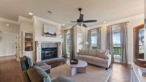 Un salón comedor amplio con chimenea, ventilador de techo y un gran ventanal con cortinas.