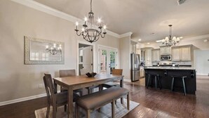 Una cocina amplia con una isla central, mesa de comedor de madera y una araña.