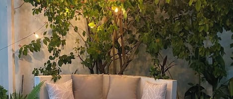 A curved bench with a cushion, surrounded by greenery and string lights.
