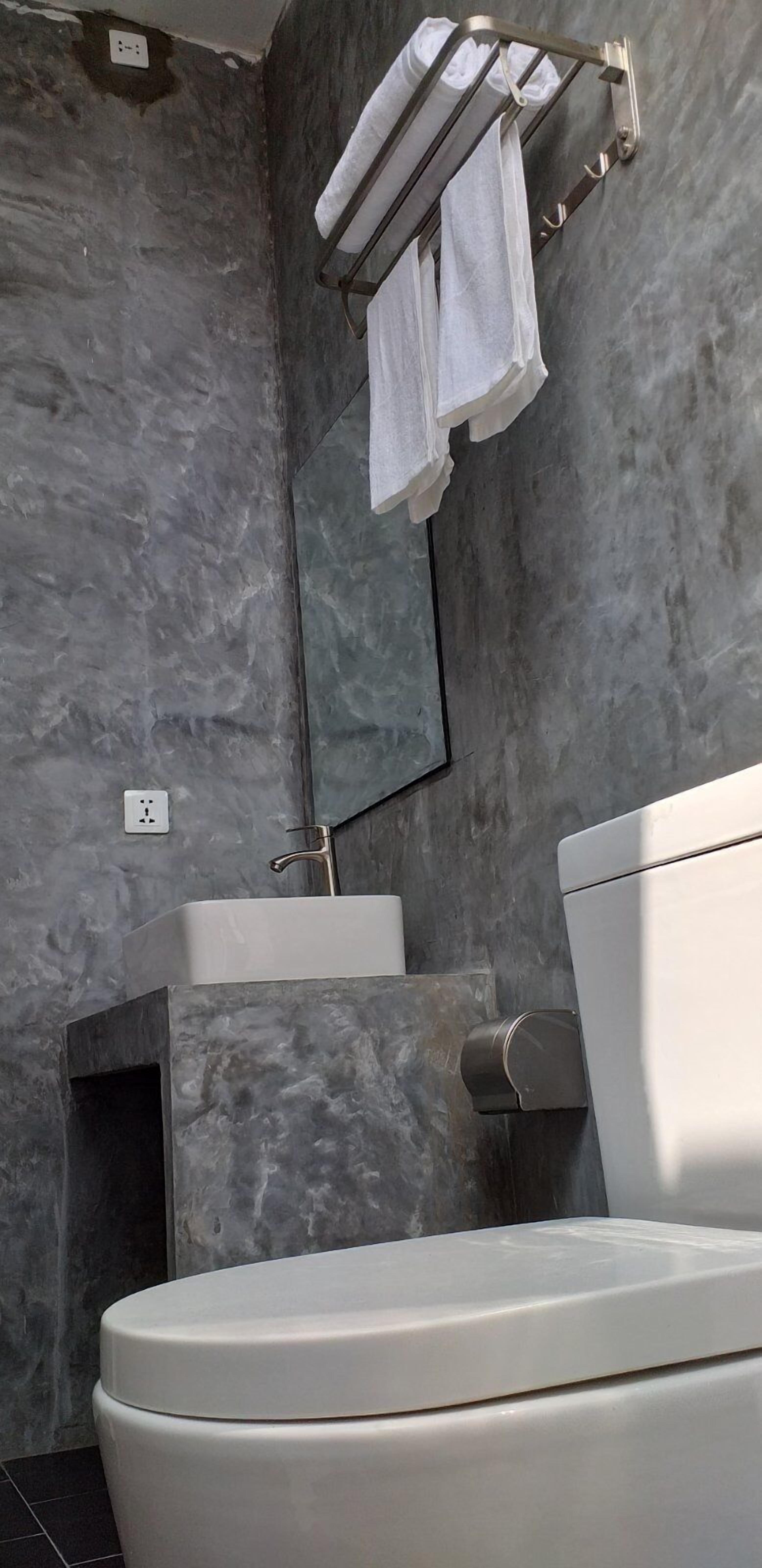 Un baño moderno con pared de mármol, un lavamanos blanco, un inodoro y un perchero con dos toallas.