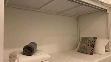 A single bed with a white mattress and a rolled-up towel on the left side. There is a pillow with a floral pattern on the right side of the bed.