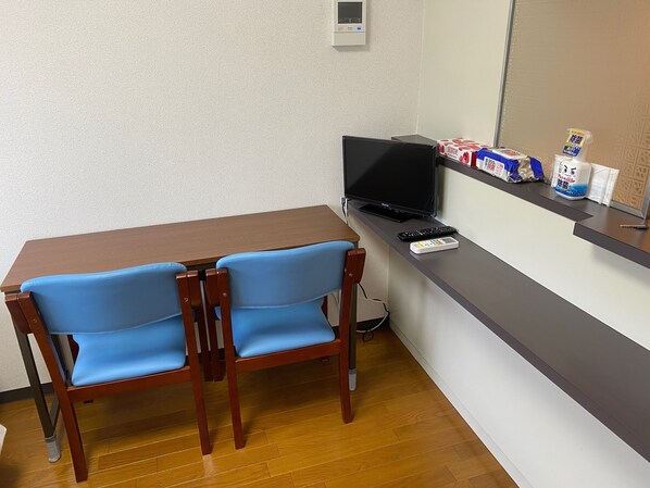 A small room with a wooden table and two blue chairs, a black TV on a stand, a remote control, and some cleaning supplies on the counter. - W312 Tokyo Monthly Rentals - Great Area Komazawa (Setagaya City)