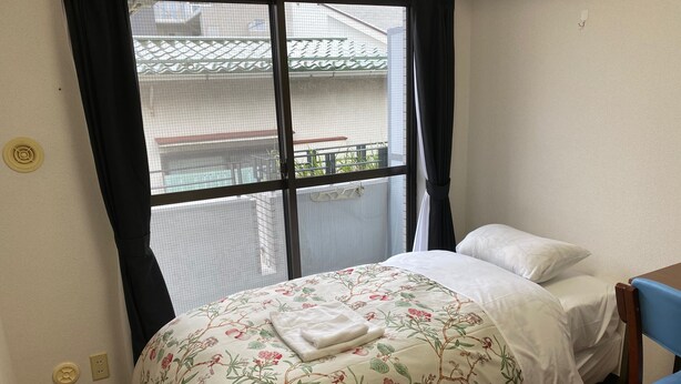 A bedroom with a bed, a chair, a window with a view of a balcony, and a door. - W311 Tokyo Monthly rental- Sakurashinmachi Sunrise (Setagaya City)