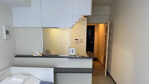 Une chambre d’hôtel de taille réduite, comprenant un lit, une kitchenette et une petite salle de bain.