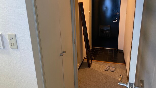 Un couloir étroit, avec une porte fermée au bout, une paire de chaussons sur le sol et un interrupteur sur le mur.