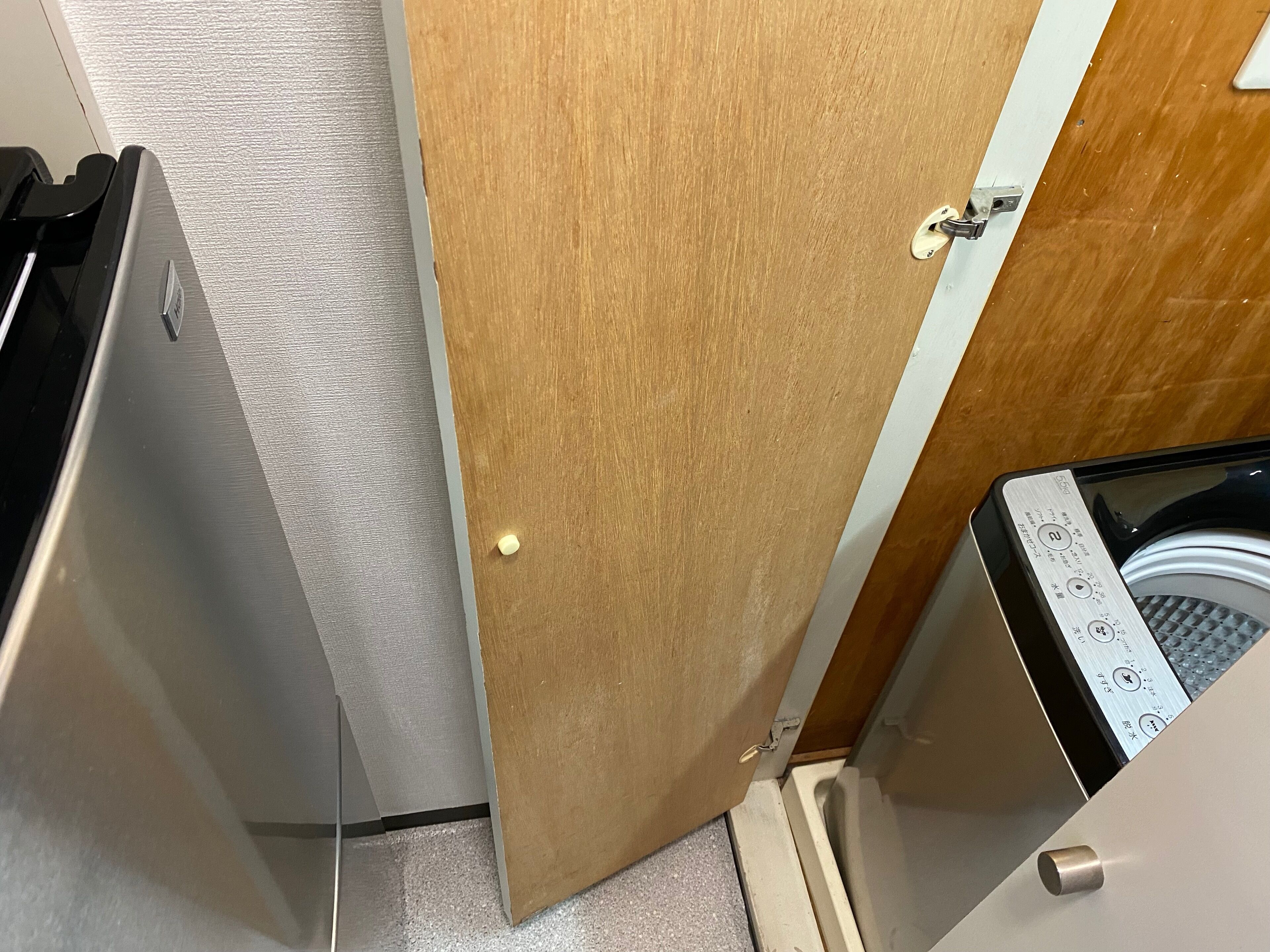 Un baño pequeño con puerta de madera, toallero blanco y lavadora.