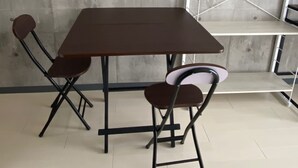 Ein Raum mit einem dunkelbraunen Tisch, vier Stühlen, einem Metallregal und einer Betonwand.