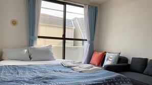 A bedroom with a bed, a sofa, and a window with curtains. - W306 Monthly Rental Tokyo - Sunrise Living (Setagaya City)