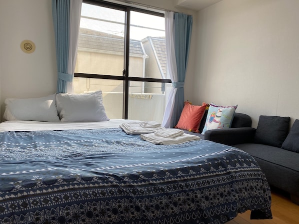 A bedroom with a bed, a sofa, and a window with curtains.
