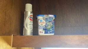 Une étagère sur laquelle se trouvent deux produits d’hygiène : un flacon de détergent Attac Zero et un emballage de lessive Ariel Bio.
