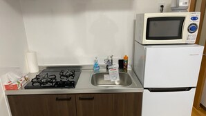 A compact kitchen with a gas stove, a sink, a microwave, and a refrigerator. - W212 Tokyo Monthly Rental - Komazawa Telework (Setagaya City)