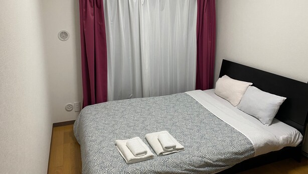 A hotel room with a bed, white and black patterned bedspread, two pillows, and a pair of folded towels. - W212 Tokyo Monthly Rental - Komazawa Telework (Setagaya City)
