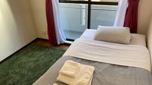 A hotel room with a checkered bedspread, white pillows, and a green rug. - W210 Tokyo Monthly Rental - Sakurashinmachi Single (Setagaya City)