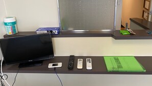 A hotel room with a television, remote controls, a mobile phone, and a green folder on a desk. - W210 Tokyo Monthly Rental - Sakurashinmachi Single (Setagaya City)
