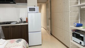 Une cuisine compacte équipée d’un four à micro-ondes, d’une cuisinière et d’un réfrigérateur. On y trouve également un petit four et une étagère sur laquelle est posée une boîte.
