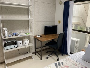 A hotel room with a wooden desk, a black office chair, a television, and a shelf with a kettle, a hairdryer, and a spray bottle. - W207 Tokyo Monthly Rental - Sakurashinmachi Reno (Setagaya City)