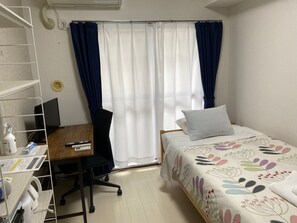 A hotel room with a bed, a desk with a chair, a computer, and a shelf with various items. - W207 Tokyo Monthly Rental - Sakurashinmachi Reno (Setagaya City)
