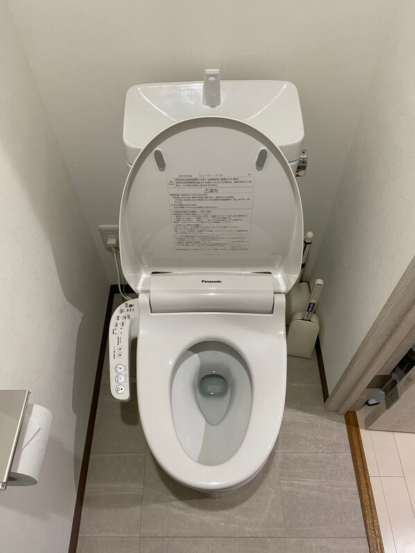 A toilet with a control panel, a toilet brush, and a paper towel holder. - W207 Tokyo Monthly Rental - Sakurashinmachi Reno (Setagaya City)